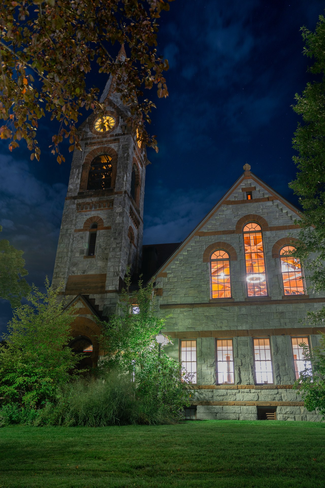 A warmly lit stone building and tower framed by trees at night