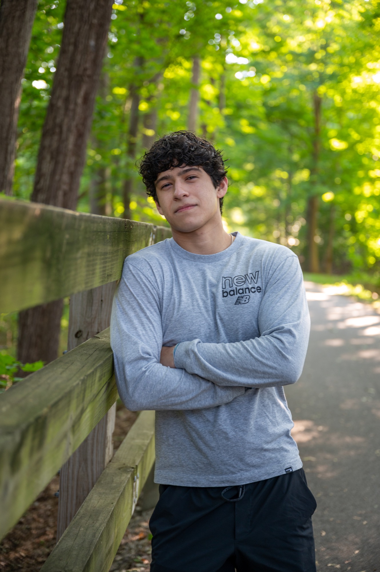 Portrait beside a wooden fence with sunlight filtering through green trees